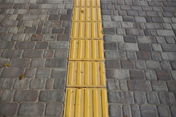 Yellow tactile tiles for the blind and visually impaired on the sidewalk in the city on the street