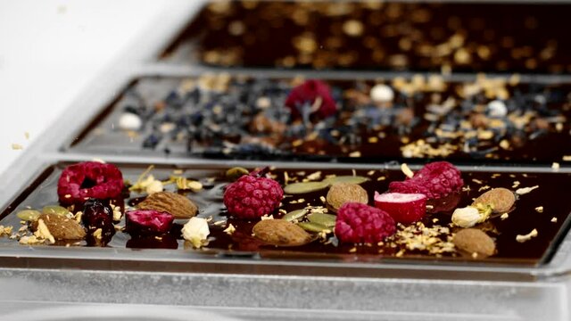 Close-up decorating of exclusive handmade chocolate bars with natural ingredients and spices. Making delicious dark organic hand-crafted chocolate, small chocolate factory, confectionery, slow motion