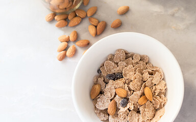 Disfruta de un saludable y delicioso desayuno acompañado con frescas almendras y un bowl de cereales vistos desde un ángulo levemente elevado y sobre una encimera de mármol gris. 