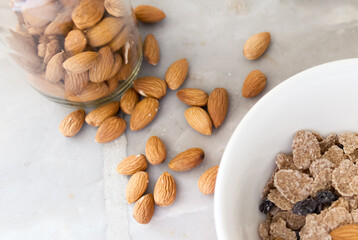 Disfruta de un saludable y delicioso desayuno acompañado con frescas almendras y un bowl de cereales vistos desde un ángulo levemente elevado y sobre una encimera de mármol gris. 
