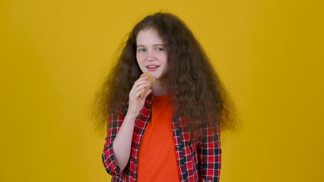Happy girl with curly hair in shirt eating ice cream isolated on yellow studio background