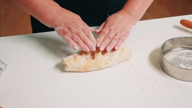 Closeup shot of hands of senior bakery kneading dough. Retired elderly baker with bonete mixing ingredients with sifted wheat flour forming on a floured surface for baking traditional cake, bread