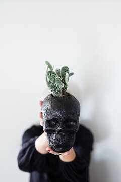 Woman hiding behind a black skull planter containing a cactus