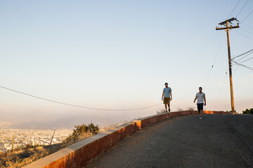 Two young men friends walking on a road at sunset with scenic view of city at sunset