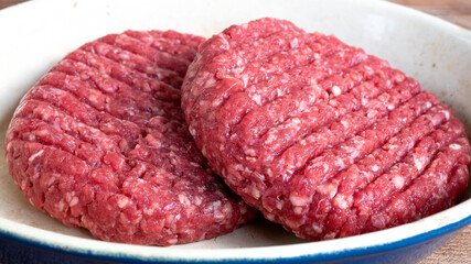 Two raw hamburger patties that are lightly seasoned with salt and pepper, sitting outside in order to reach room temperature before putting them on the grill. Raw meat and food preparation concept.