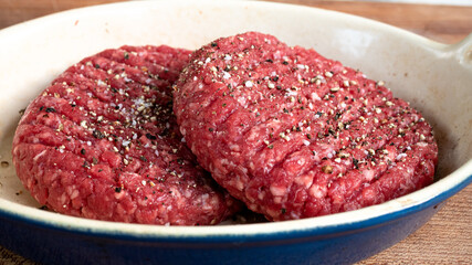 Two raw hamburger patties that are lightly seasoned with salt and pepper, sitting outside in order to reach room temperature before putting them on the grill. Raw meat and food preparation concept.