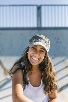 Smiley teen-age girl black sweater sits in a skate park.