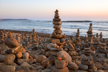 Beach with several balanced stone towers built by people at sunset