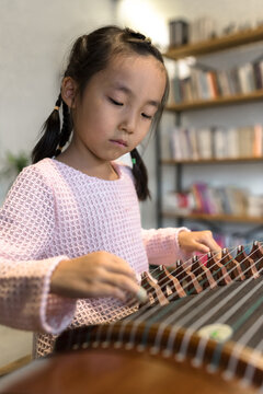 Adorable little girl playing zither at home