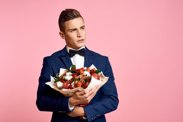 Handsome man in a classic suit with a bouquet of flowers on a pink background holidays bow tie model