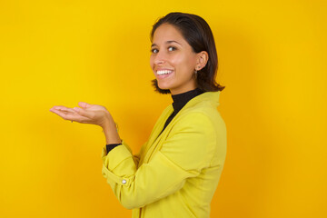 Young hispanic businesswoman wearing casual turtleneck sweater and jacket pointing aside with hands open palms showing copy space, presenting advertisement smiling excited happy