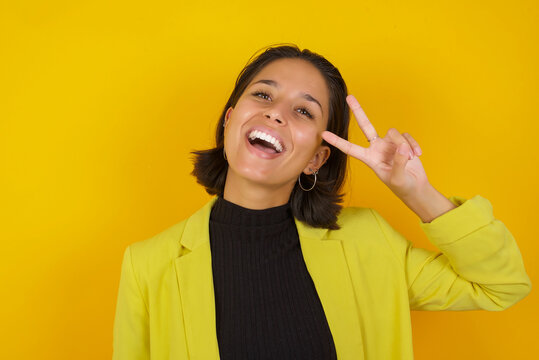 Young hispanic businesswoman wearing casual turtleneck sweater and jacket Doing peace symbol with fingers over face, smiling cheerful showing victory