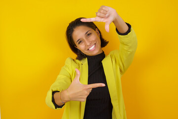 Young hispanic businesswoman wearing casual turtleneck sweater and jacket making finger frame with hands. Creativity and photography concept.