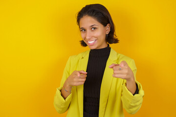 Young hispanic businesswoman wearing casual turtleneck sweater and jacket pointing fingers to camera with happy and funny face. Good energy and vibes.