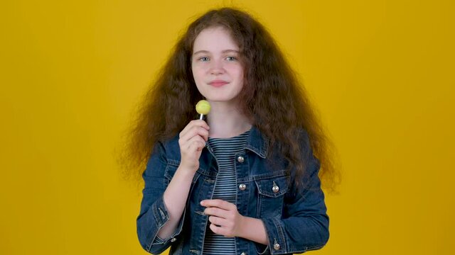 Portrait of young girl with curly hair with candy isolated on yellow background