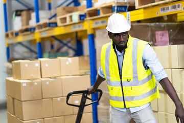 Black Male warehouse worker pulling a pallet truck. middle aged African American warehouse worker preparing a shipment in large warehouse distribution centre © NVB Stocker