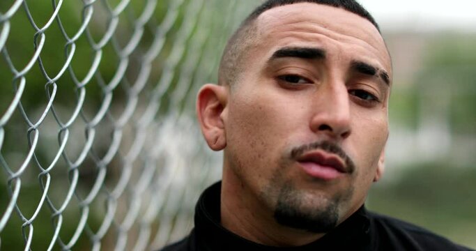 Pensive hispanic man leaning on metal fence looking at camera. Latin guy portrait