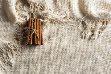 A set of cinnamon sticks tied with natural jute string on a tablecloth with fringe. Horizontal image with space for text.