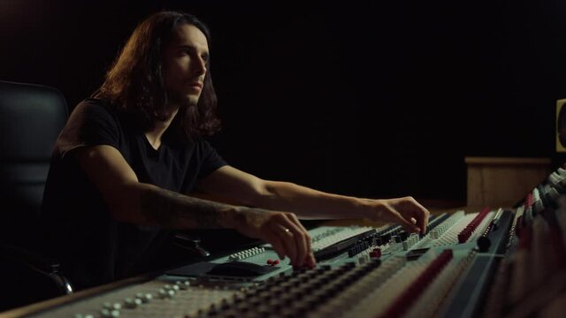 Thoughtful man working in music studio. Composer moving sliders indoor.