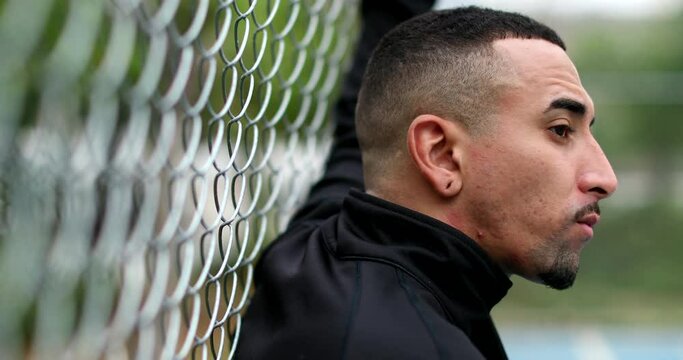 Pensive hispanic man leaning on metal fence thinking