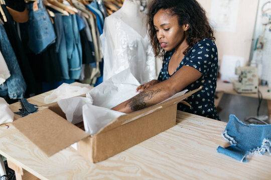 Young female business owner fashion entrepreneur packing clothing in box subscription delivery service