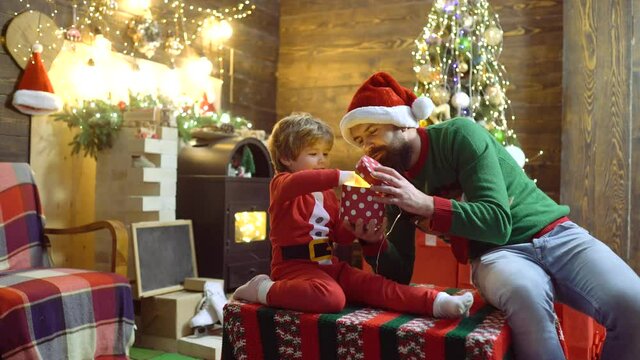 Father and son prepare at Christmas. Dad and child hold Xmas prasent gifts at home. Kid with parent giving presents and enjoy New Year. Magic light.