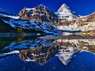 Hiker person walking along the Lake Magog with Mount Assiniboine in the background, British Columbia, Canada