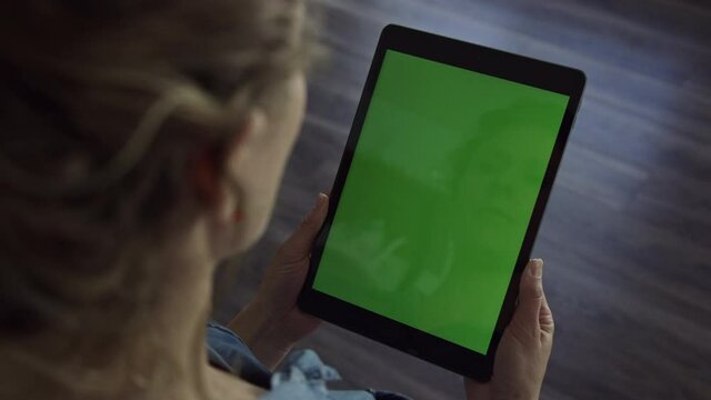 Woman holds tablet device in portrait orientation with blank green screen