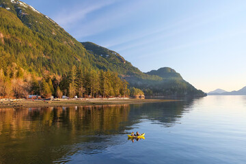 Obraz premium Sea kayaking with yellow kayak at Canadian coast during sunset, Porteau Cove, Vancouver, British Columbia