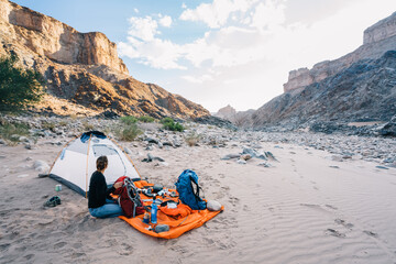 Woman with her camping gear unpacked outside her tent in a desert canyon