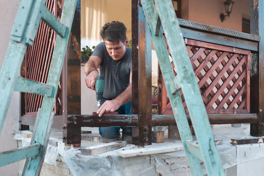 Man drilling small plank on wooden built structure outdoor