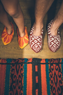 father and son in colorful handknitted shoes beside handmade colorful carpet on wooden floor from above
