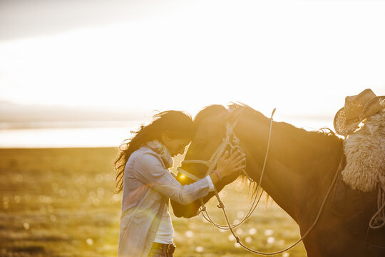 sensitive young woman is head on head with her horse at sunset