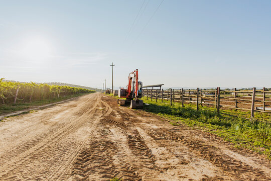 Bulldozers parked at farm's roadside close to vineyard and pasture corral at sunset