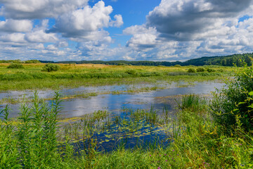 Stunning landscape with river, field, haystacks and gorgeous clouds in the sky