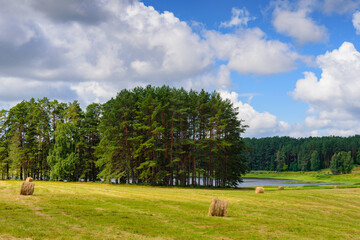 Stunning landscape with a lake, field, haystacks and gorgeous clouds in the sky