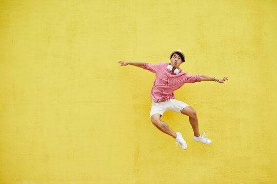 Jumping hipster in hat with headphones over yellow background.