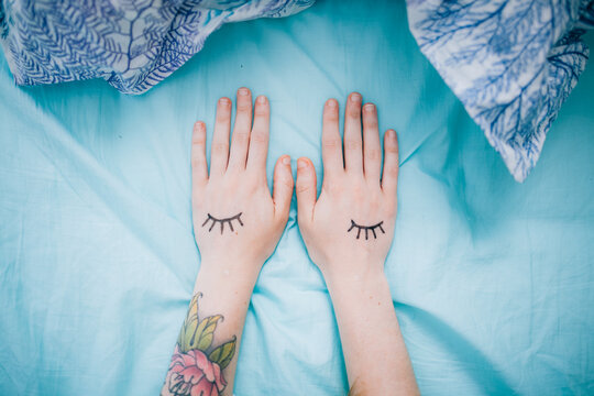 hands with drawn eyelashes on blue sheets