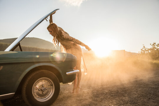 A pretty young woman trying to fix her classic car