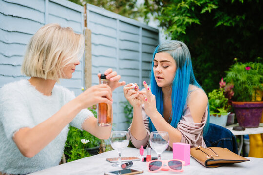 two friends sitting together painting fingernails while listening to music on bluetooth speaker