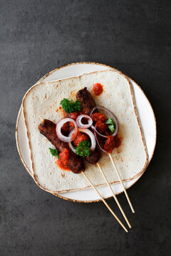 Cevapcici on wooden skewers with onions, parsley and ajvar.