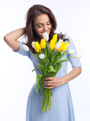 Beautiful girl in the blue dress with flowers tulips in hands on a light background