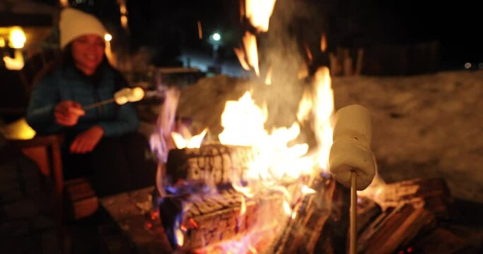 Winter Holiday Ski Resort Woman Roasting Marshmallows In BBQ Firepit. Afterski Fun Activity With Friends. Couple Grilling Marshmallow On Stick In Fire