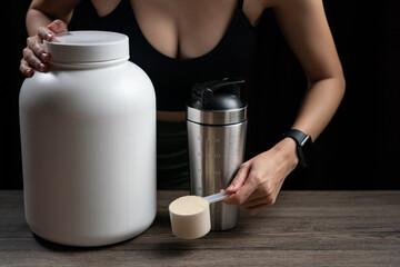 Close up of women with measuring scoop of whey protein, jar and shaker bottle, preparing protein shake.