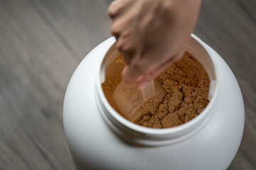Woman's hands holding measuring scoop of whey protein powder over jar.