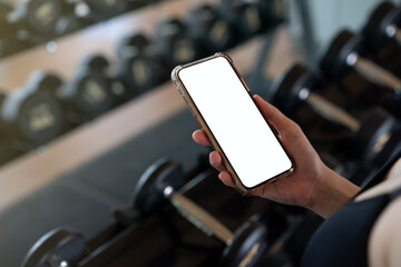 Woman hand holding mobile phone with blank white screen mockup in gym.