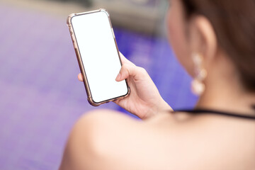 Woman hand holding mobile phone with blank white screen mockup by the pool.