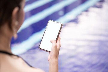 Woman hand holding mobile phone with blank white screen mockup by the pool.