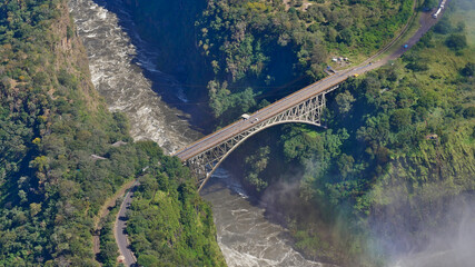 Aerial view of famous Victoria Falls Bridge, marking the border of Zimbabwe and Zambia (Africa), over Zambesi River with the spray of the waterfalls from helicopter.