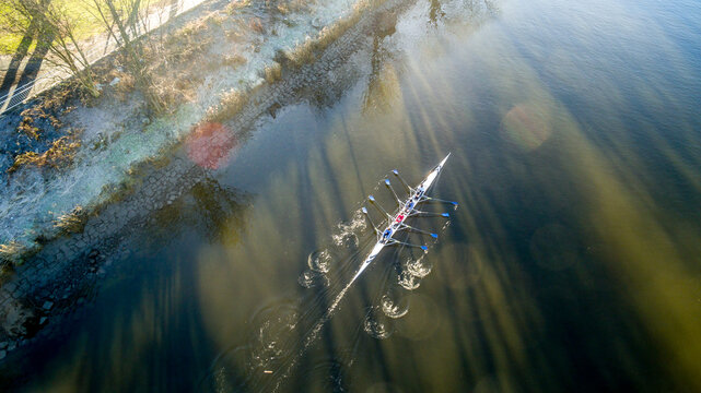 A crew of rowers race down a river in cold spring sunshine